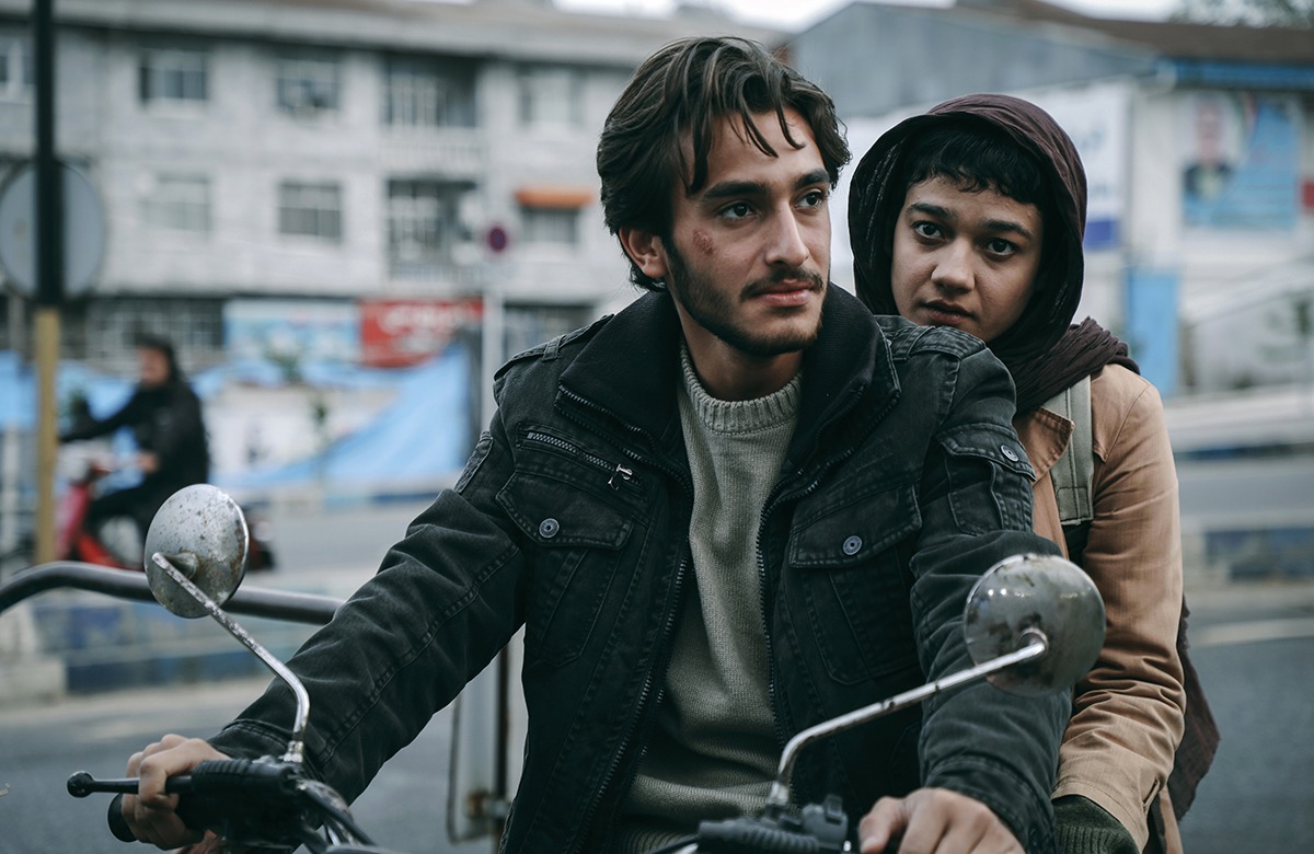 A man and a woman sitting on a motorcycle in a city.