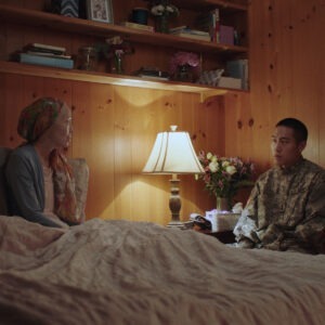 A soldier and woman sitting on a bed.