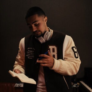 A man wearing headphones and a jacket holding a pen and notebook.