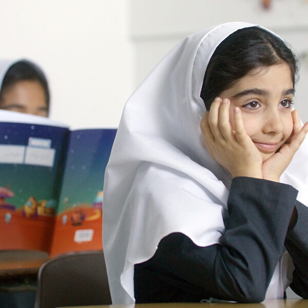 A girl in a hijab sits at a desk and reads a book.