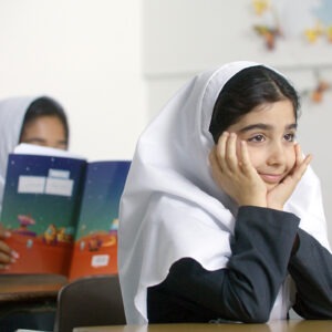 A girl in a hijab sits at a desk and reads a book.
